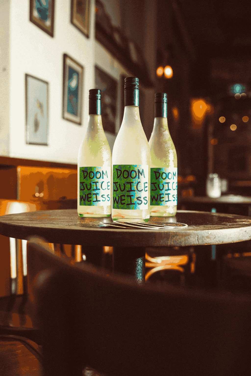 Three bottles of 'Doom Juice Weiss on a wooden table in a bar setting.
