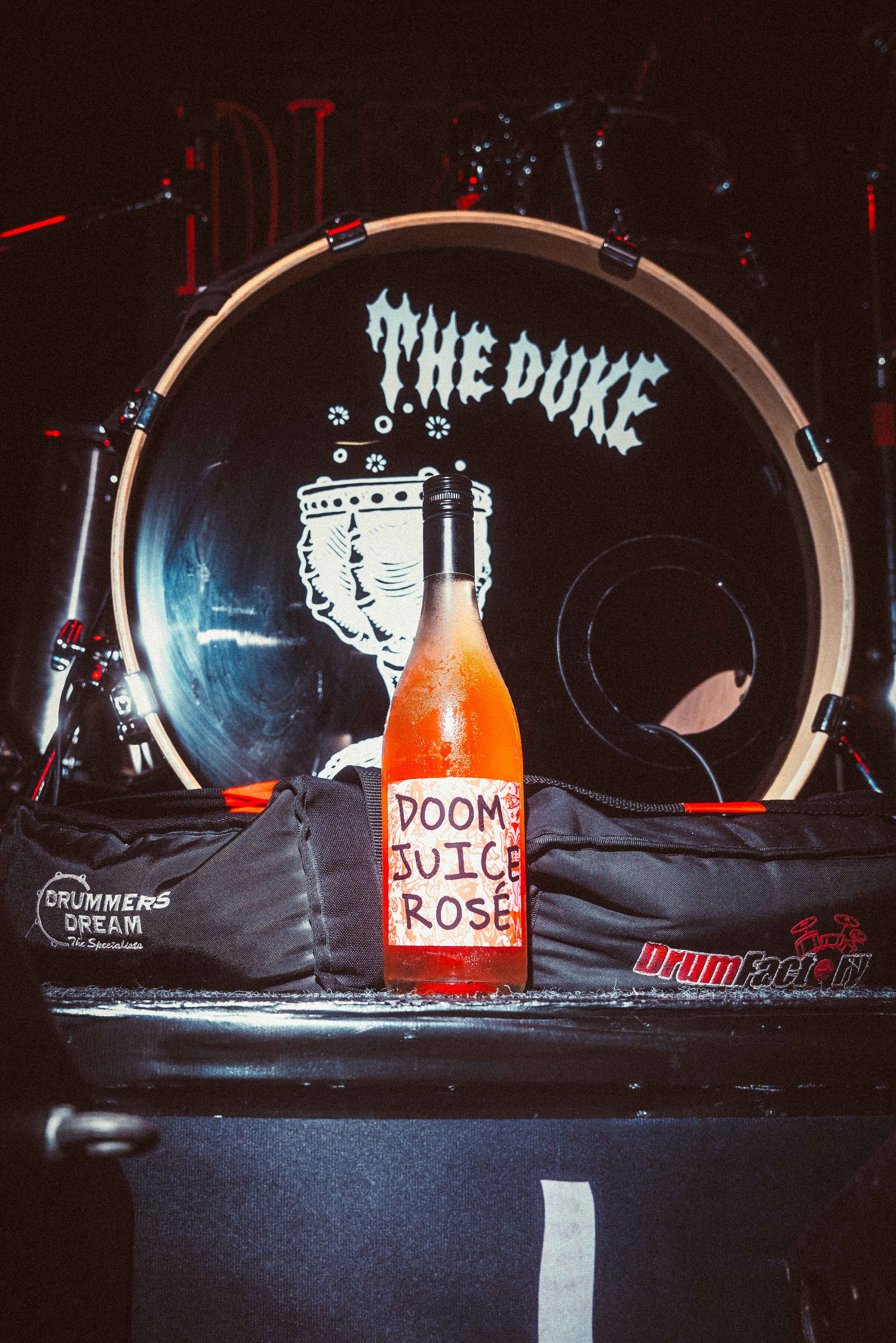 Bottle of 'Dooms Juice Rose' on a drum set with 'The Duke' branding.