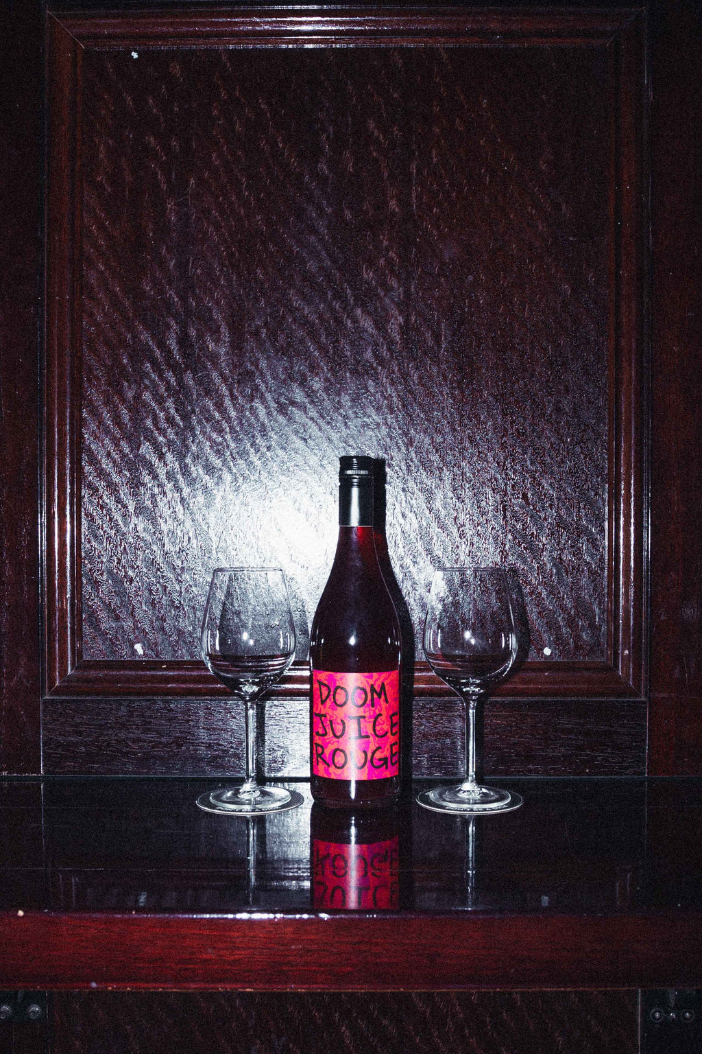 Wine bottle with a red label on a bar counter with glasses in front of a dark background