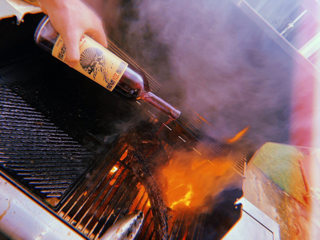 Person pouring a Doom Juice wine from a bottle onto a grill with flames.