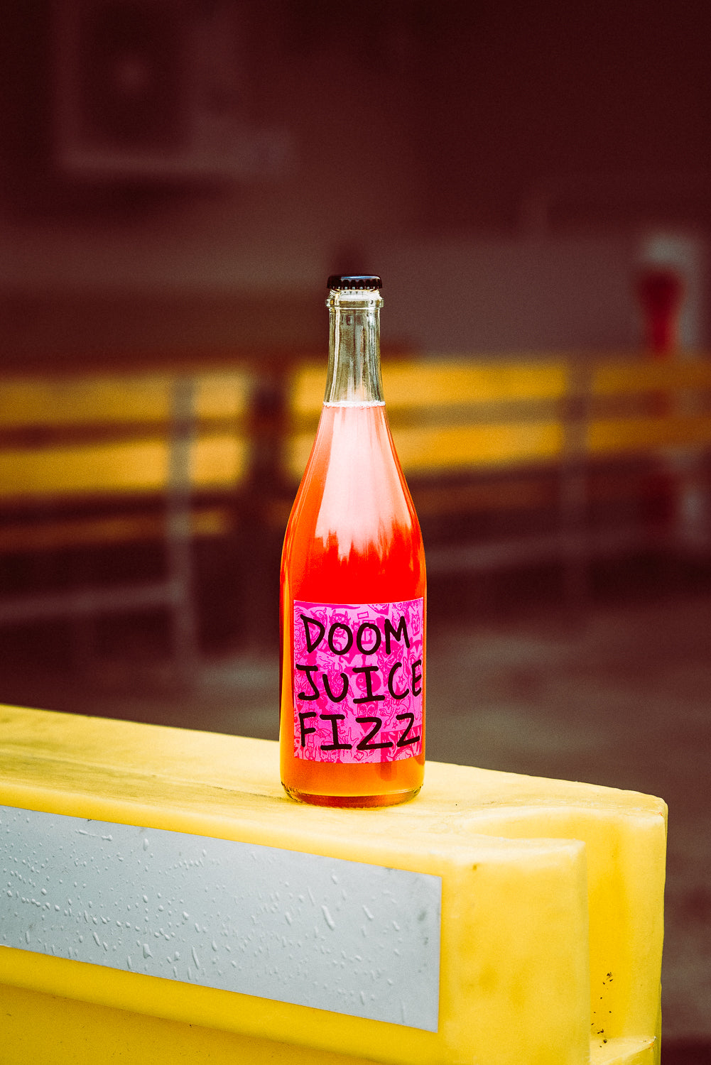 Bottle of 'Doom Juice Fizz' on a yellow surface with a blurred background