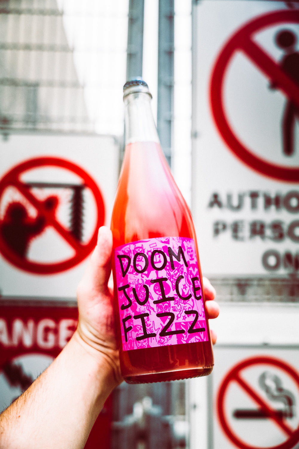 Hand holding a bottle labeled 'Doom Juice Fizz' in front of warning signs.