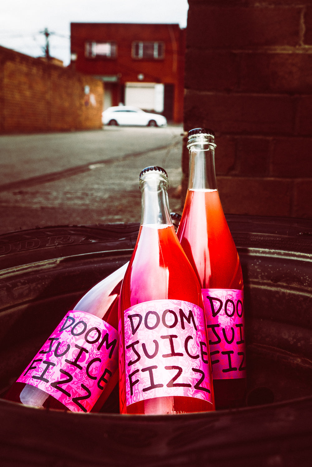 Two bottles of 'DOOM JUICE FIZZ' on a metal surface with a street and building in the background.