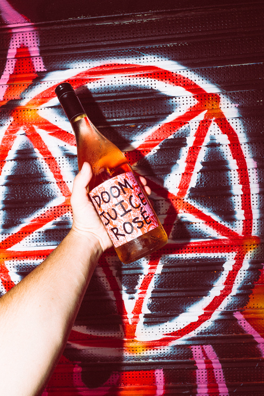 Bottle of Doom Juice Rose held by a hand against a colourful background