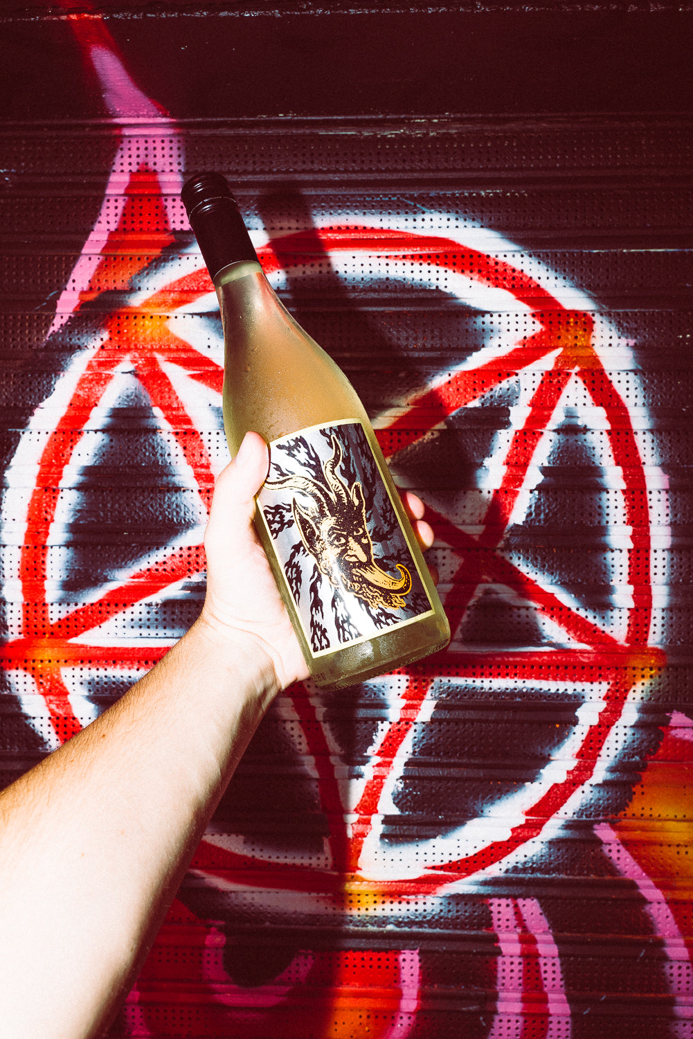 Hand holding a bottle with a graphic design against a colorful abstract background