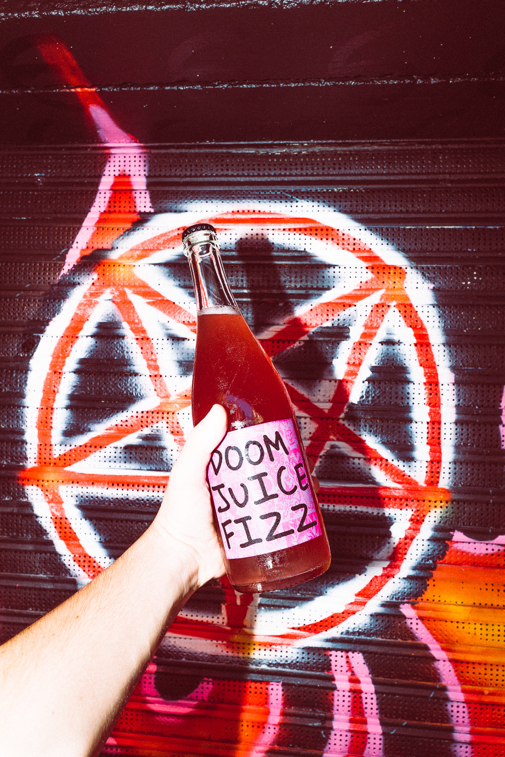 Person holding a bottle labeled 'Doom Juice Fizz' in front of a colorful abstract background