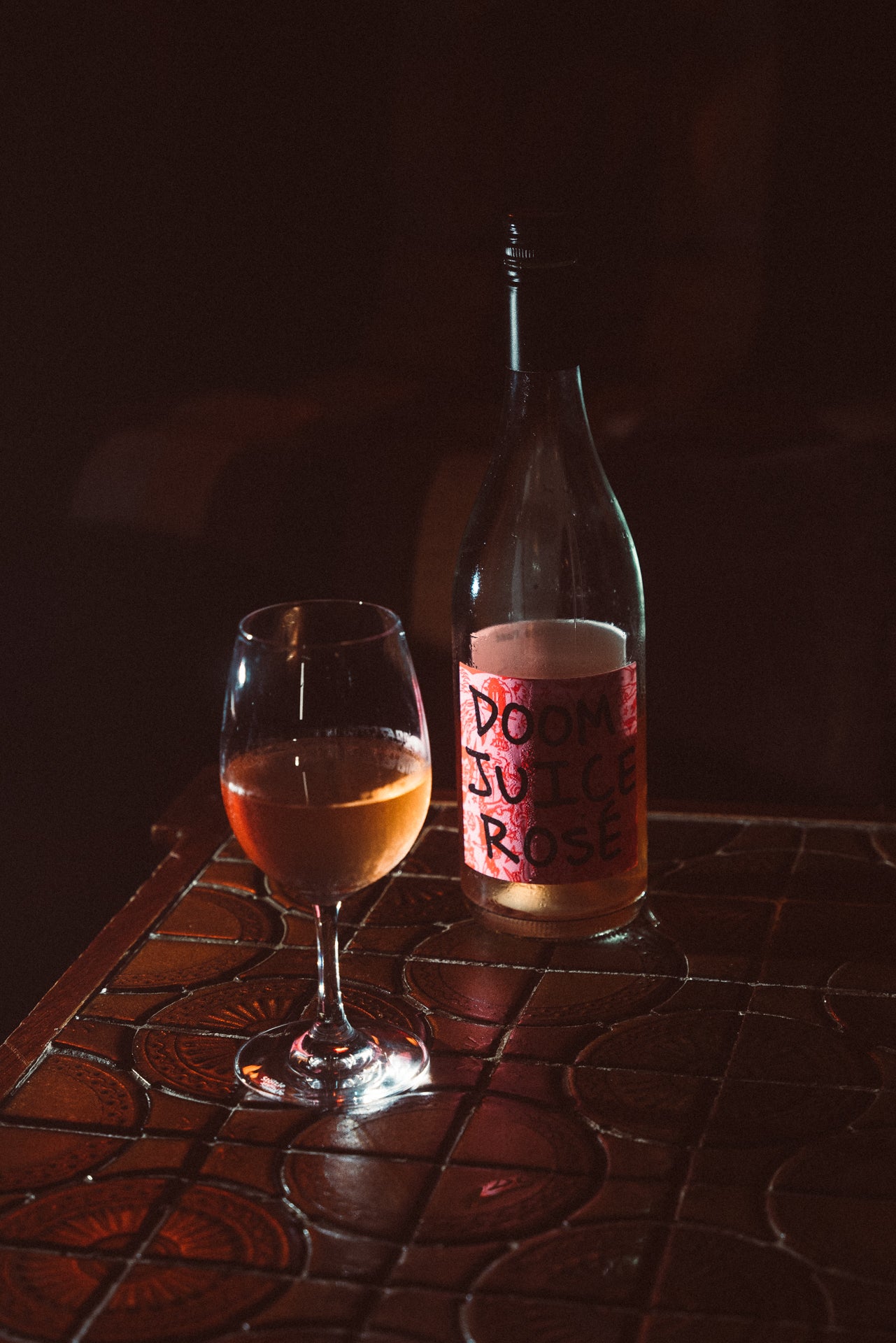Bottle and glass of Doom Juice Rose on a textured surface with a dark background