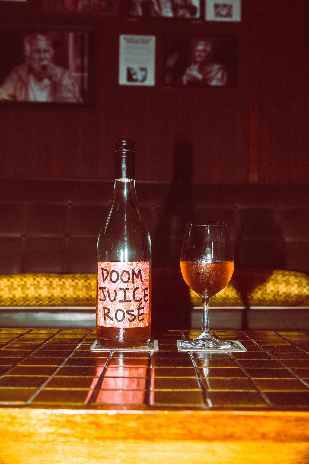 Bottle of 'Doom Juice Rosé' with a glass of wine on a bar counter.