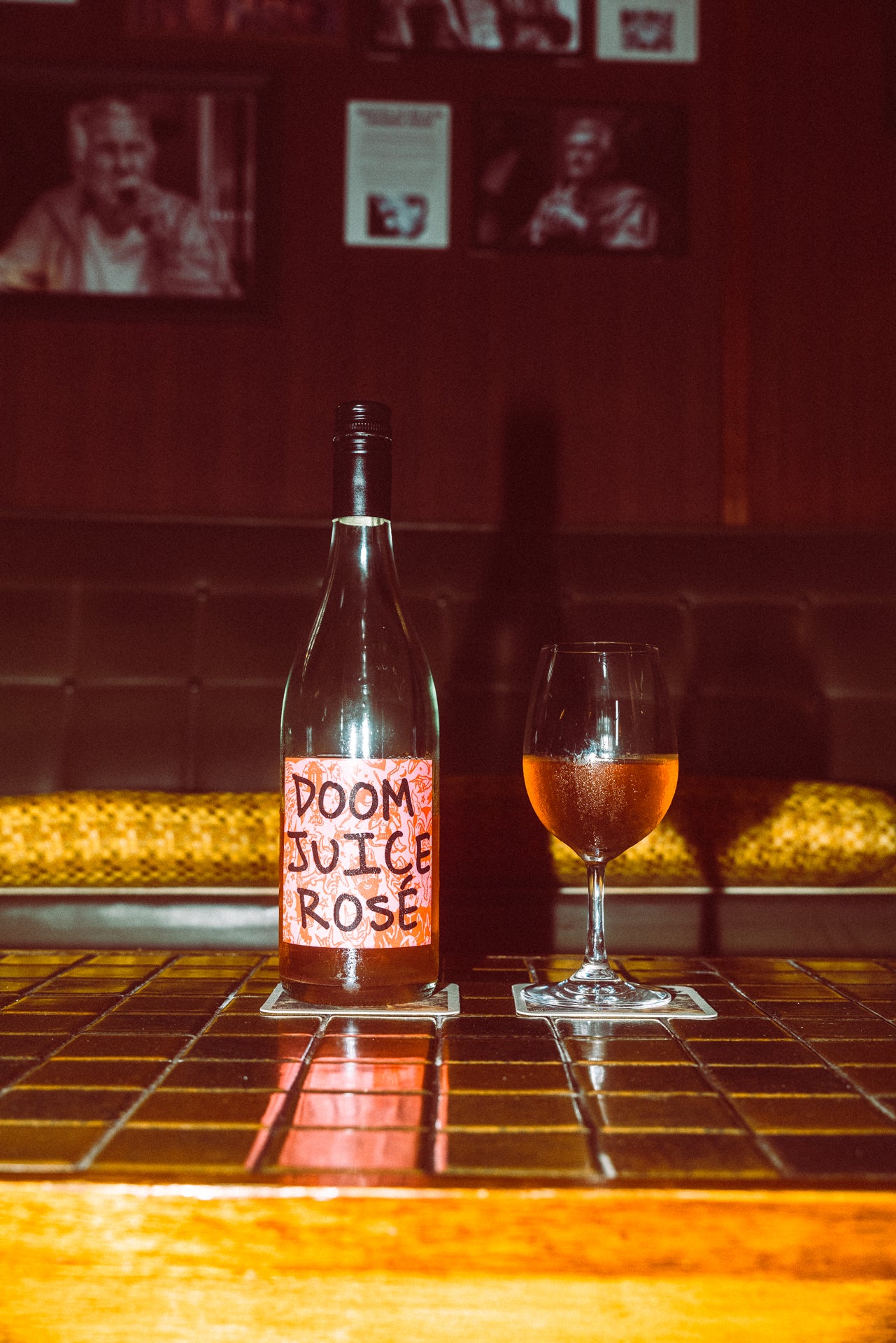 Bottle of 'Doom Juice Rosé' with a glass of wine on a bar counter.