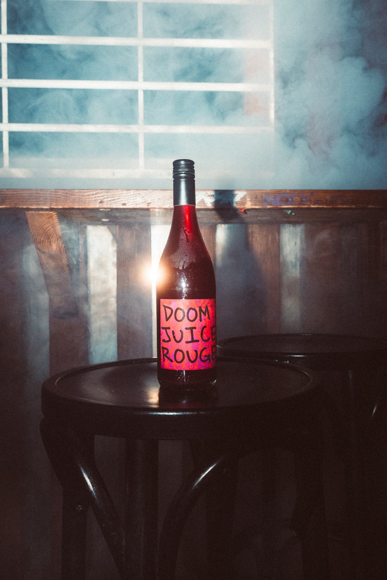 Bottle labeled 'Doom Juice Rouge' on a dark surface with a blue and white abstract background