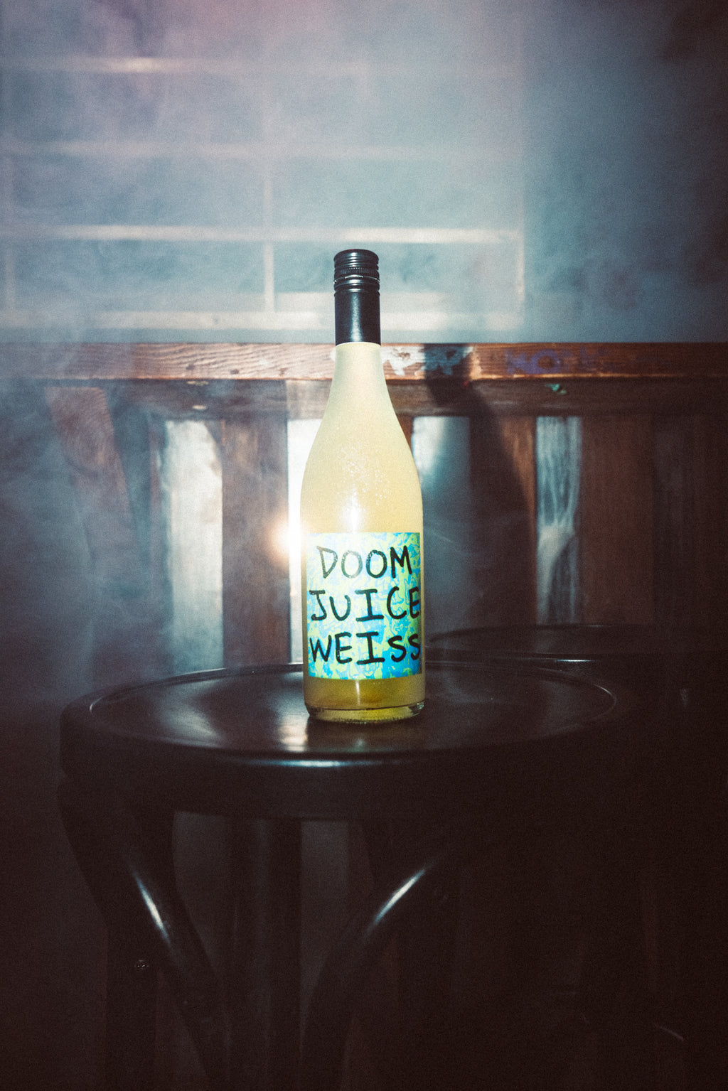 Bottle of 'Doom Juice Weiss' on a wooden stool with a textured wall background